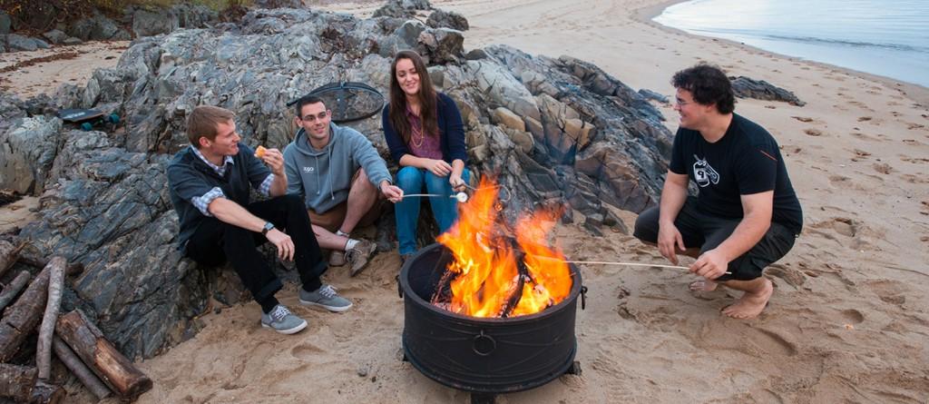 a group of students sit around a bonfire on the beach