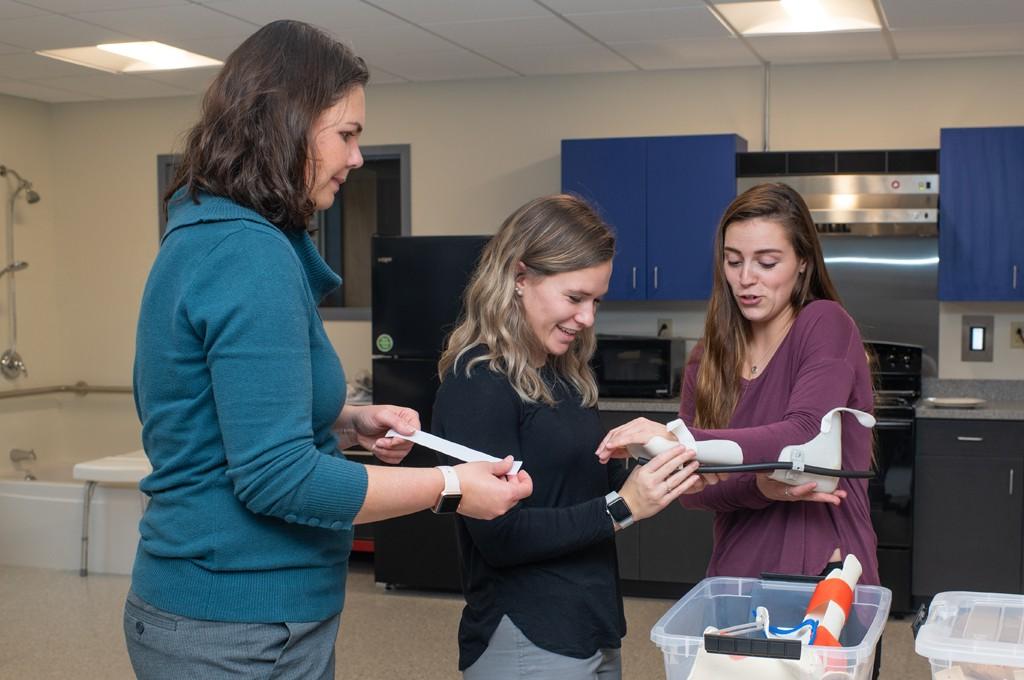 Two U N E Occupational Therapy students working with a professor in the O T Lab