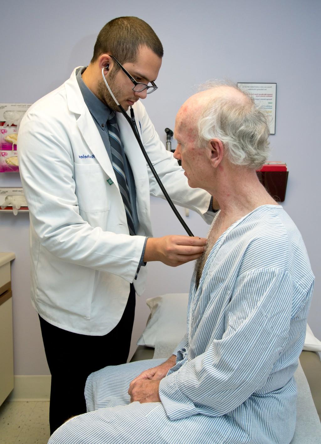 A C O M student uses a stethoscope to listen to an elderly patient's heartbeat and breathing
