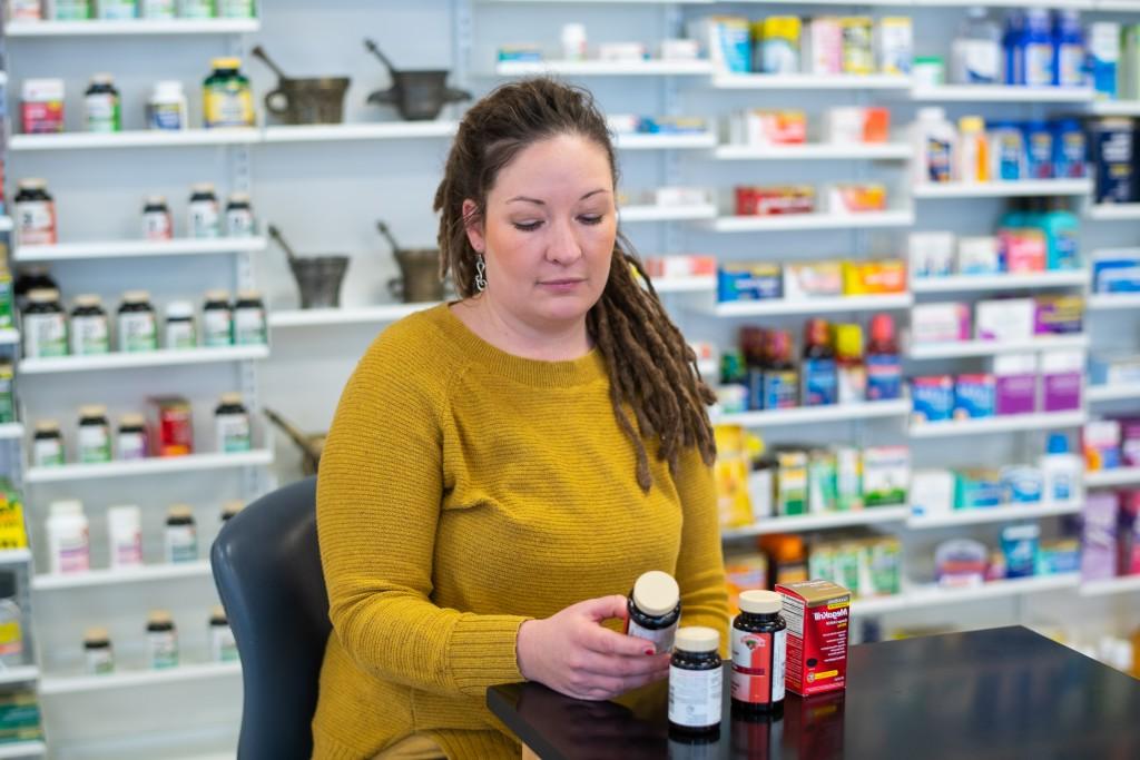 A pharmacy student sits in front of a wall of medicine bottles and is reviewing the ingredients on a pill bottle