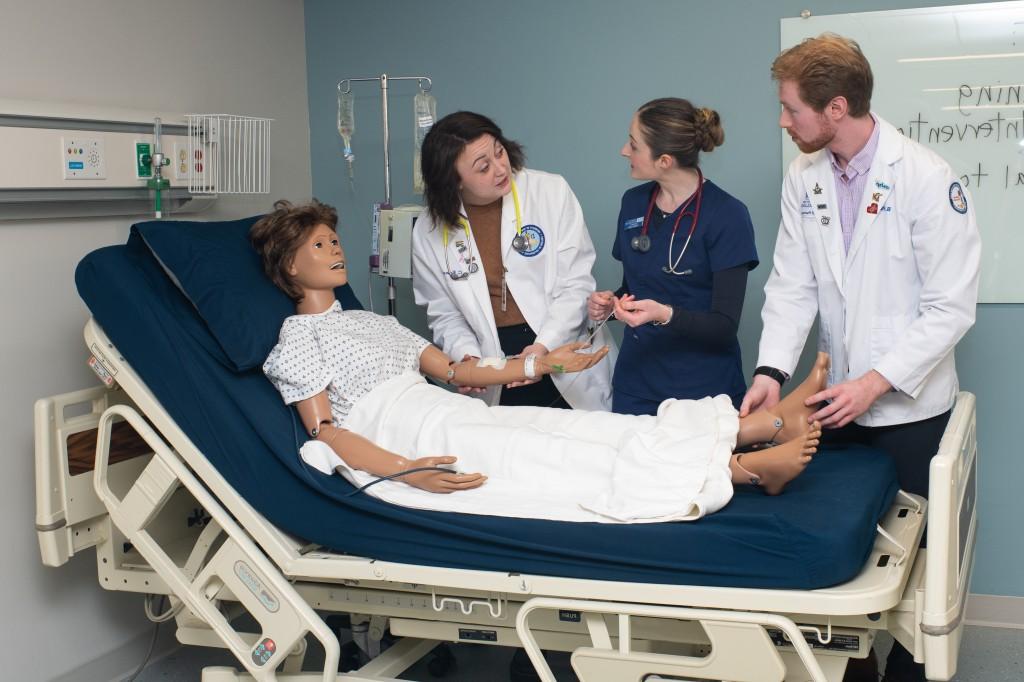 Two C O M students and a nursing student practice working together on a simulated patient