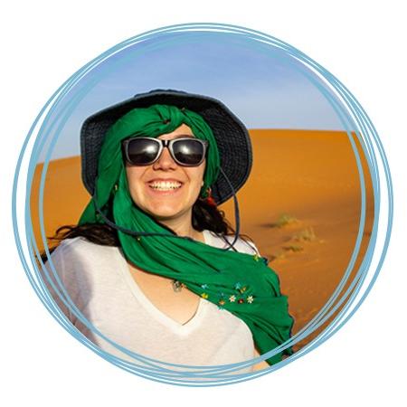 一名学生戴着绿色围巾、遮阳帽和太阳镜站在摩洛哥沙漠中微笑