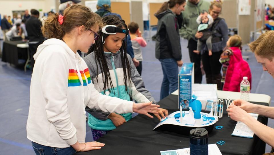 在联合国大脑博览会上，一个戴着科学设备的孩子和她的朋友一起学习它的使用方法
